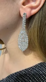 Aros colgantes de diseño alargado en forma de gota, completamente cubiertos de cristales brillantes engarzados en metal plateado.