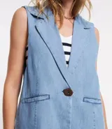 Chaleco largo de jean celeste con escote en pico y cierre con un botón marrón.