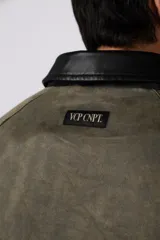 Chaqueta de estilo militar color verde oliva, confeccionada en gabardina resistente. Presenta cuello camisero en contraste color negro, cierre frontal con cremallera, dos bolsillos frontales tipo cargo con solapa y ajuste relajado.