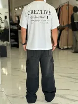Remera oversize color beige, con diseño estampado en la espalda que incluye tipografía grande y texto descriptivo en negro.