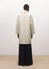 Chaqueta larga de algodón color beige, de diseño recto, manga larga, cuello camisero y cierre delantero con botones ocultos. Cuenta con dos bolsillos laterales con solapa.