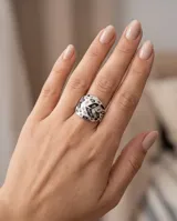 Anillo de acero de diseño amplio con patrón geométrico esmaltado en tonos blancos, negros y grises, y detalles de nácar.