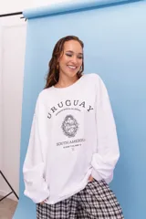 Buzo oversize de cuello redondo en color blanco, con estampa frontal gráfica que incluye el escudo nacional, la palabra Uruguay y coordenadas geográficas.