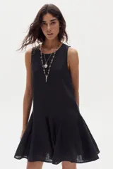 Vestido corto de lino negro, sin mangas, con cuello redondo y diseño evasé con godets en el ruedo que aportan movimiento.