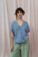 Blusa de lino color fucsia, con escote en V y manga corta amplia. Presenta un detalle de botón decorativo dorado en el centro del escote.