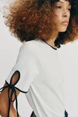 Camiseta de algodón de corte regular, color blanco con detalles de vivos y lazos en contraste negro en el cuello y en las mangas cortas.