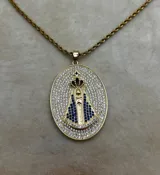 Collar con cadena tipo soga dorada y un dije ovalado grande con la figura de la Virgen María. La medalla está enchapada en oro y completamente incrustada con circones blancos, mientras que la figura de la Virgen tiene detalles en circones azules.