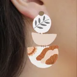 Aros colgantes con diseño abstracto en tonos tierra y blanco, con forma geométrica y herrajes plateados.