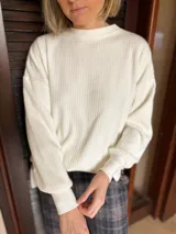 Sweater de punto acanalado en color natural, con cuello redondo, mangas largas con puños ajustados y diseño holgado con aberturas laterales en el ruedo.