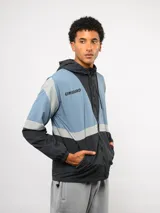Campera de nylon Umbro con capucha, cierre frontal y diseño de bloques de color en gris, blanco y azul. Puños y dobladillo elásticos.
