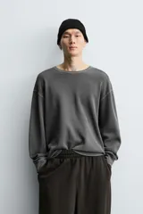 Camiseta de manga larga con cuello redondo, confeccionada en tejido de algodón con textura tipo waffle y efecto lavado. Presenta un corte relajado con puños en rib y bajo irregular.