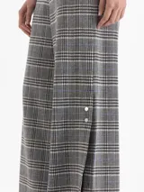 Pantalón de tiro alto con corte amplio y relajado, confeccionado en tejido de punto con estampado de cuadros tipo príncipe de gales. Presenta cintura elástica, bolsillos laterales con broches metálicos y botamangas amplias.