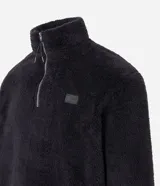 Buzo de tejido peludo color negro, con cuello alto y cierre frontal parcial. Presenta mangas largas con puños elásticos, bolsillo tipo canguro y etiqueta decorativa en el pecho.