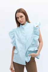 Chaleco celeste de lino con cuello mao y cierre frontal con botones. Presenta volados en los hombros y bolsillos con volados en el frente.