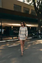Blazer de cuello redondo y manga larga, con diseño a cuadros en tonos beige, azul y negro. Presenta cierre frontal cruzado con botones metálicos y corte recto.