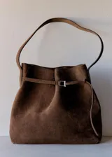 Bolso tipo shopper de cuero vacuno en color marrón oscuro, con diseño estructurado, cierre superior con solapa y hebilla metálica, y correas de hombro integradas.