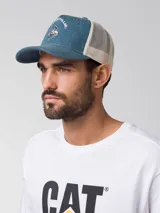 Gorro tipo trucker de color azul denim en la parte frontal y visera, con malla trasera blanca. Presenta un estampado frontal con la inscripción "Caterpillar" y la silueta de un vaquero montando un caballo. Incluye cierre trasero ajustable.