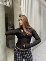 Polera de manga larga confeccionada en tela de encaje negro con textura geométrica. Presenta un diseño ajustado al cuerpo con cuello alto y acabado semitransparente.