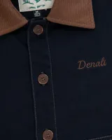 Campera estilo workwear de color azul oscuro, confeccionada en canvas resistente con interior de corderito sherpa. Presenta cuello de pana en color marrón, cierre frontal con botones metálicos color cobre, dos bolsillos frontales amplios y bordado de la marca en el pecho.