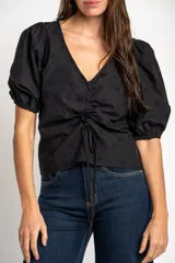 Blusa negra de algodón con diseño bordado sutil, escote en V y cordón ajustable fruncido en el centro del frente. Mangas cortas abullonadas.