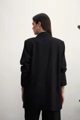 Blazer de mujer color rosa pálido, de corte recto y largo, con solapas de muesca y un solo botón frontal marrón. Presenta bolsillos de parche en la parte delantera y mangas tres cuartos.