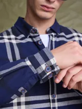 Camisa de manga larga en color azul noche con un patrón de cuadros finos en tonos rojos y verdes. Presenta cuello clásico, cierre frontal con botones y un bolsillo en el pecho con solapa.