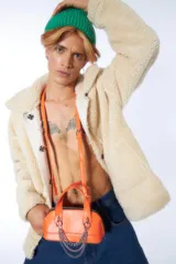 Cartera de mano naranja de cuero sintético con doble asa corta, cierre superior con doble cremallera y cadena metálica plateada decorativa. Incluye correa extraíble y ajustable.