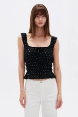 Musculosa de viscosa color negro con estampado de lunares blancos, tirantes anchos con volados fruncidos, escote cuadrado con cordones ajustables en el centro y cuerpo elástico con punto smock.