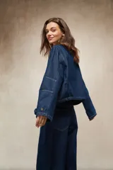 Sobrecamisa de denim azul oscuro, con cuello de pana color camel, cierre frontal de cremallera y dos bolsillos frontales con tapa y botón.