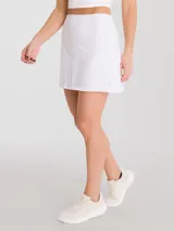 Falda deportiva blanca con calza interior incorporada, diseñada con tejido de secado rápido. Presenta un diseño levemente acampanado con detalle plisado en la parte trasera, pretina con bolsillo con cierre y bolsillo adicional en la calza interior.