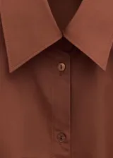 Camisa de algodón color marrón, de diseño cruzado estilo sobre con lazo lateral para anudar, cuello camisero, manga larga y calce amplio.