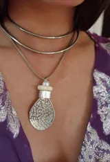 Collar plateado con dos gargantillas rígidas y un colgante con forma de lágrima con textura de alpaca.