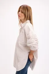 Camisa de corte oversize con estampado de rayas verticales finas en color marrón sobre fondo blanco. Presenta cuello clásico, cierre frontal con botones, bolsillo en el pecho y mangas largas con puños abotonados.