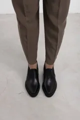Botín asimétrico de estilo Chelsea color bordó, confeccionado en cuero vacuno, con paneles elásticos laterales negros, puntera cuadrada, suela de plataforma y tacón de bloque cuadrado.