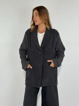 Saco color gris oscuro con cuello solapa, cierre de botones frontales y bolsillos laterales. Las mangas tienen un diseño de punto acanalado.
