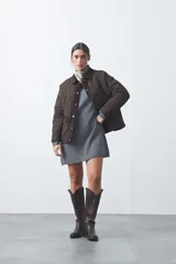 Campera tipo barn capitoneada de color marrón, con silueta corta y relajada. Presenta cuello de pana, cierre frontal con broches metálicos y bolsillos laterales funcionales.