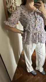 Camisa estampada con cuello bebé y mangas cortas abullonadas con volantes. Presenta tres lazos para cerrar en el frente y corte con volantes en la cintura.