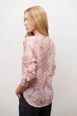 Camisa de manga larga con cuello redondo y cierre frontal de botones. Presenta un estampado floral en tonos azules y marrones sobre una base de color rosado claro.