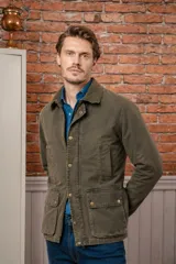 Campera encerada de estilo clásico con cuello de pana, cierre frontal con cremallera y botones a presión, y bolsillos frontales de gran capacidad.