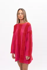 Buzo tipo poncho de tejido de punto con diseño de bloques de color en tonos rojo y fucsia. Presenta un corte oversize muy amplio, cuello redondo, mangas largas y bolsillos laterales integrados.