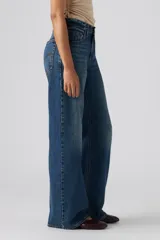 Jeans de denim azul de corte amplio y bota ancha, tiro medio, con efecto ligeramente lavado en las piernas y diseño clásico de cinco bolsillos.