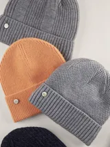 Gorro tipo beanie color azul marino, con textura de punto en relieve y borde acanalado. Incluye un pequeño aplique metálico circular con el logo de la marca en el frente.