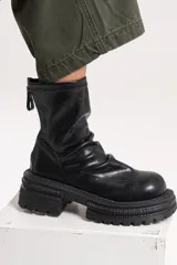 Bota de caña media con diseño robusto y contemporáneo, confeccionada en material de acabado liso. Presenta una suela chunky con relieve y cierre posterior.
