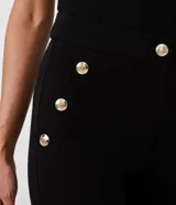 Pantalón legging negro de punto roma, con cintura alta y botones metalizados decorativos en los laterales.