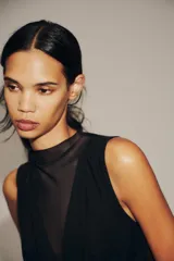 Body negro de tul con cuello alto y sisas amplias. Diseño drapeado en el frente y cierre inferior con broches a presión.