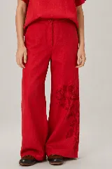 Pantalón de lino color mostaza, de corte wide leg, con sutil estampado floral en la parte inferior de la pierna izquierda y botón a la vista en la cintura.