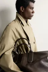 Trench regular fit de color beige, confeccionado en tejido técnico repelente al agua, con diseño de botonadura cruzada, cuello con solapas, mangas raglán con trabillas ajustables en los puños y cinturón del mismo tejido.