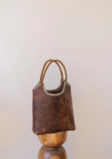 Bolso tipo matera de cuero marrón con efecto desgastado, con asas trenzadas y detalle de costura decorativa en color celeste en el borde superior.