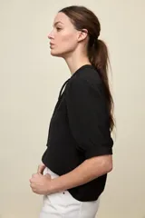 Blusa de manga corta color negro, con calce relajado, escote redondo con abertura y lazo para anudar. Presenta detalles de tablas horizontales en la parte superior que aportan textura al diseño.