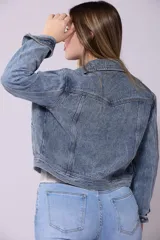 Campera de jean de mujer, color azul claro lavado, con corte cropped y estilo clásico. Presenta cuello camisero, botones metálicos frontales y bolsillos de parche en el pecho.